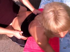 A blonde is pulling on a dick while she is outside in nature